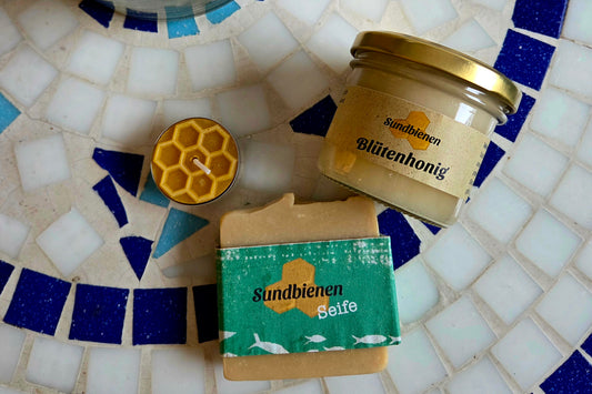 Valentinstags-Geschenkset aus der Imkerei mit einem Glas Blütenhonig, einer gelben Bienenwachskerze und handgemachter Honigseife auf Holzwolle.