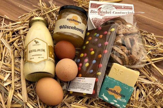 Gefülltes Osterkörbchen mit regionalen Eiern, Likör, Konfitüre und Schokolade auf Stroh.